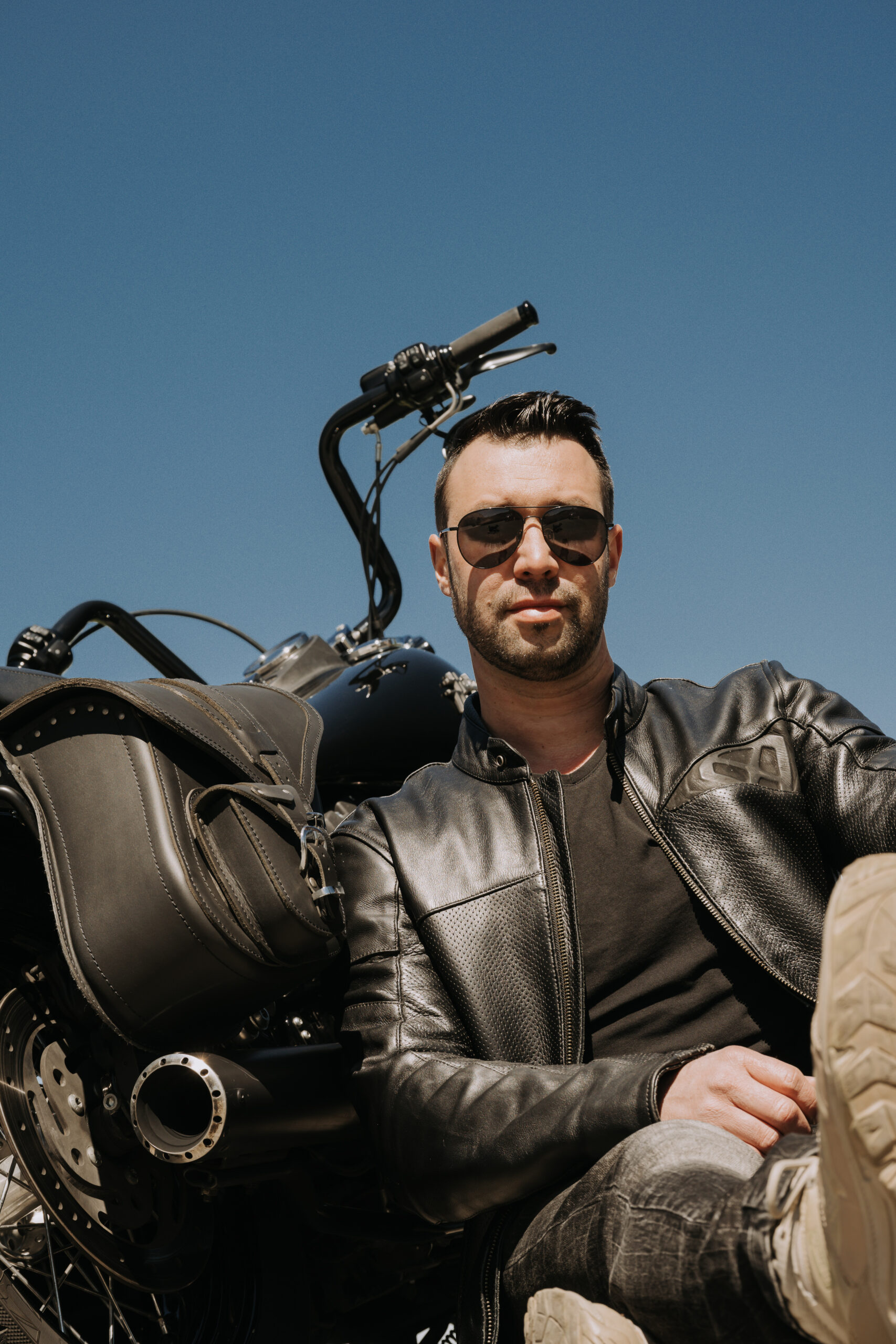 Herr sitzt neben seinem Motorrad am Boden uns lehnt sich an.
