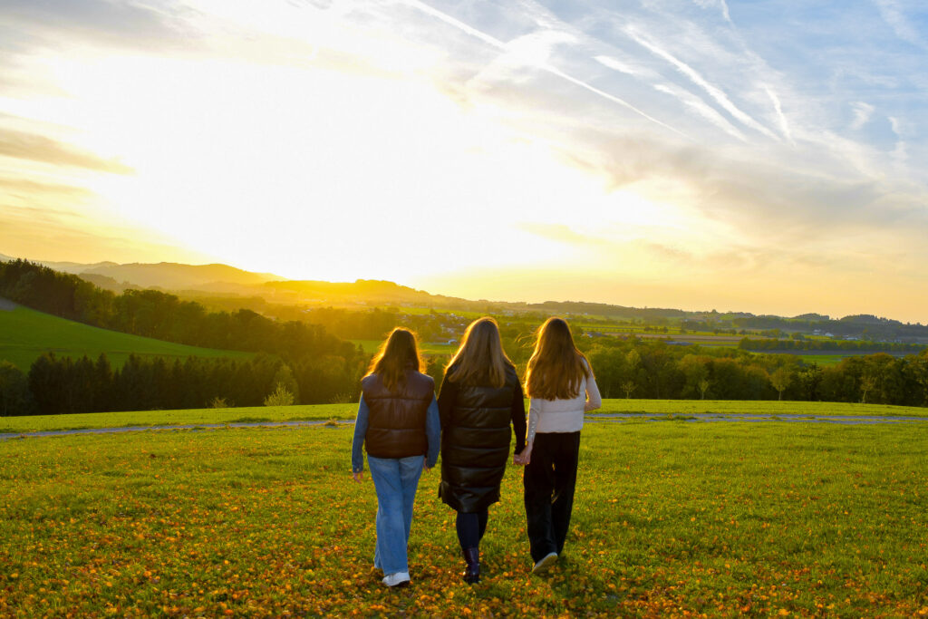 Mutter mit je einer Tochter links und rechts im Arm gehen in den Sonnenuntergang