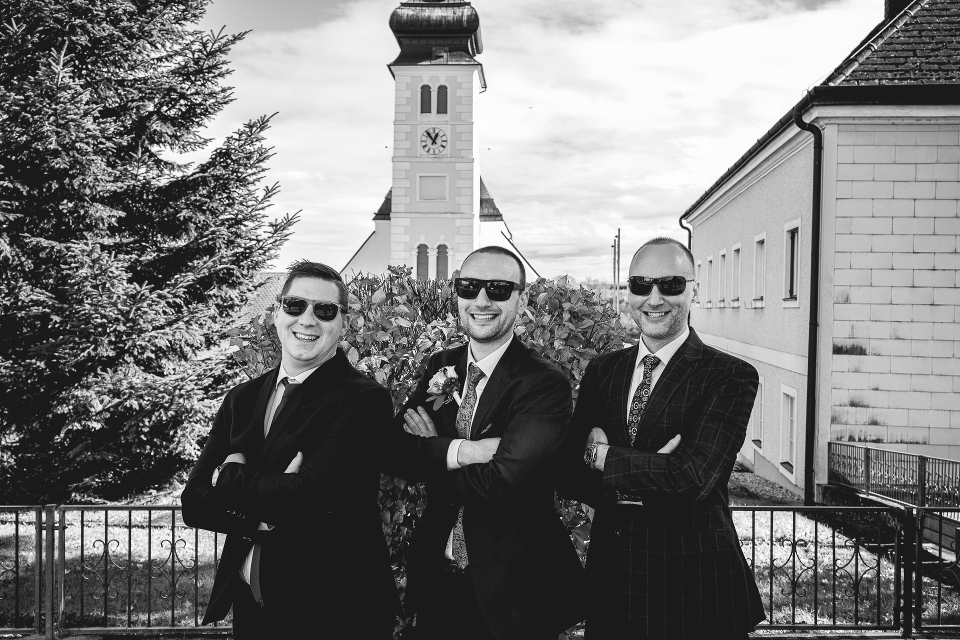 Bräutigam mit Trauzeugen vor der Kirche mit Sonnenbrillen - das Foto ist in Schwarz/Weiß