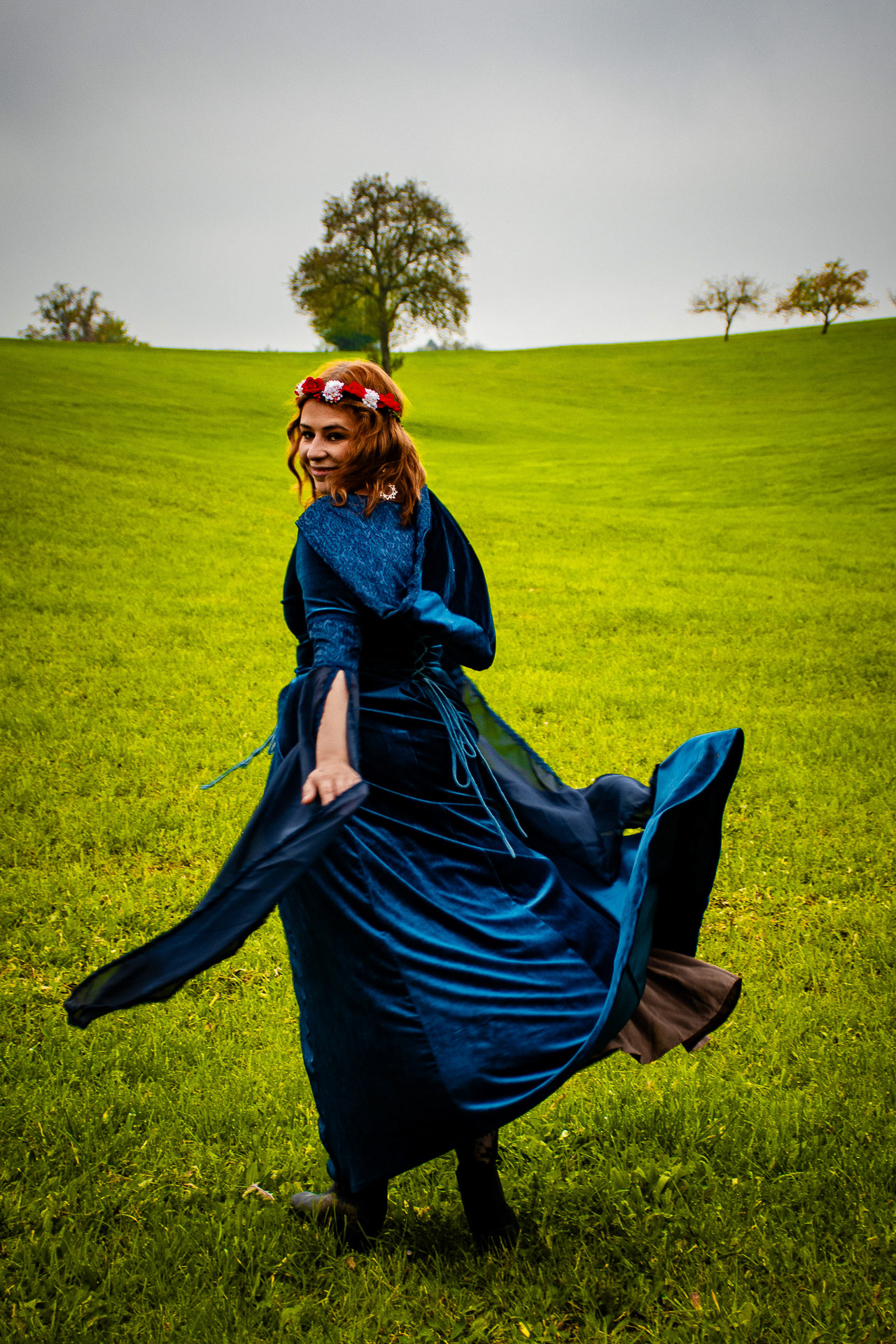 Model in Mittelalterklamotten die Blau sind läuft von der Kamera weg, dreht sich aber um und lächelt in die Kamera